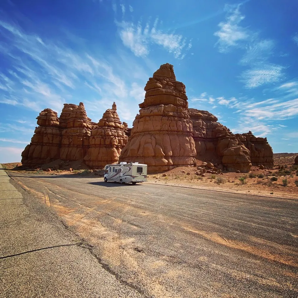 A camper van parked on an empty desert road below sandstone spires