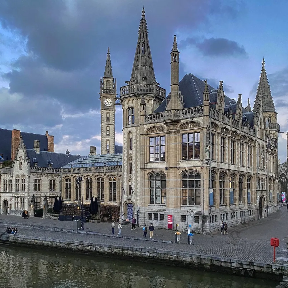 A Gothic stone building with spires standing above a canal at dusk