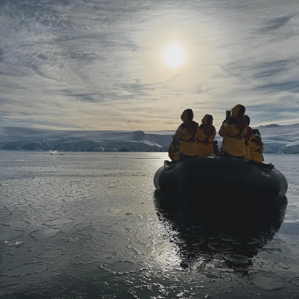 A boat of people in yellow parkas facing a low sun over pack ice